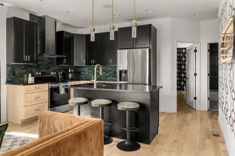 a kitchen with granite countertop a sink a stove a refrigerator and chairs