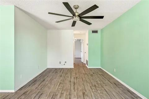 an empty room with wooden floor ceiling fan and windows