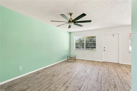 an empty room with wooden floor fan and windows