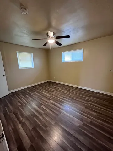 an empty room with wooden floor chandelier fan and windows