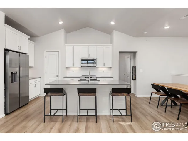 a kitchen with stainless steel appliances granite countertop a dining table chairs refrigerator and sink