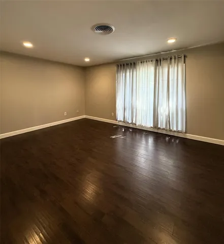an empty room with wooden floor and windows with curtains
