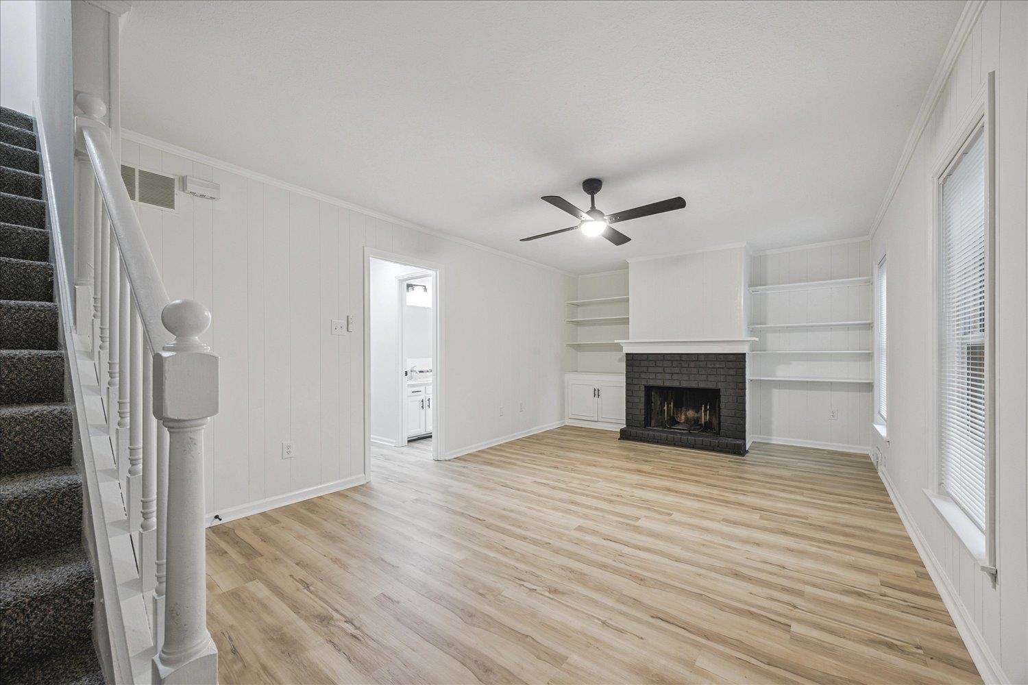 6137 Quince Road Memphis, TN 38119 - Photo 4 of 19 Unfurnished living room with crown molding, light wood-style floors, a ceiling fan, a brick fireplace, and built in shelves
