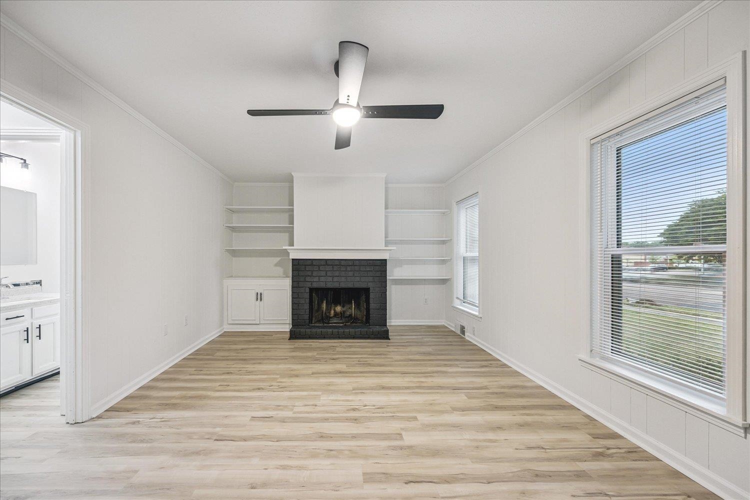 6137 Quince Road Memphis, TN 38119 - Photo 5 of 19 Unfurnished living room with light wood-type flooring, ceiling fan, a fireplace, crown molding, and built in shelves
