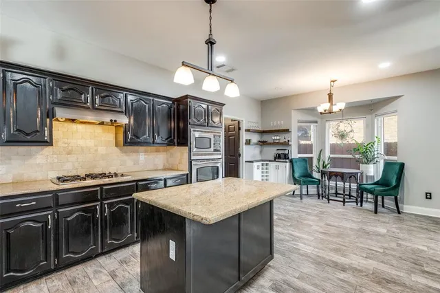 a kitchen with stainless steel appliances granite countertop a stove top oven a sink dishwasher a dining table and chairs with wooden floor