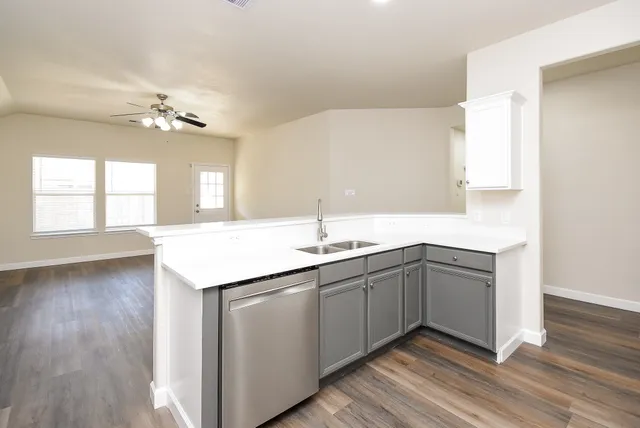 a view of an empty room with wooden floor and a kitchen