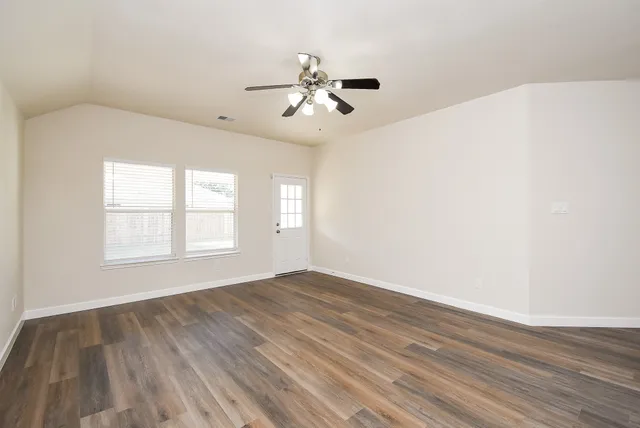 an empty room with wooden floor fan and windows