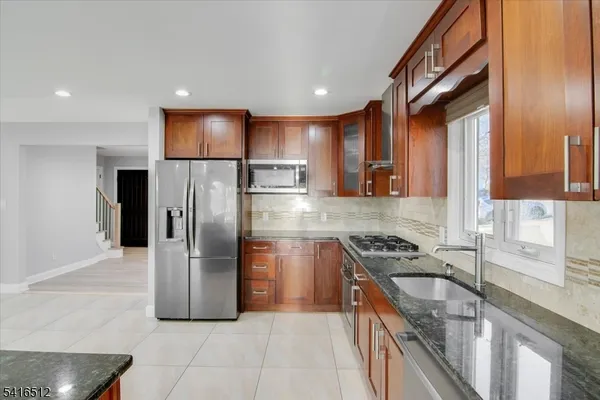 a kitchen with stainless steel appliances granite countertop a refrigerator a stove and a sink with wooden cabinets