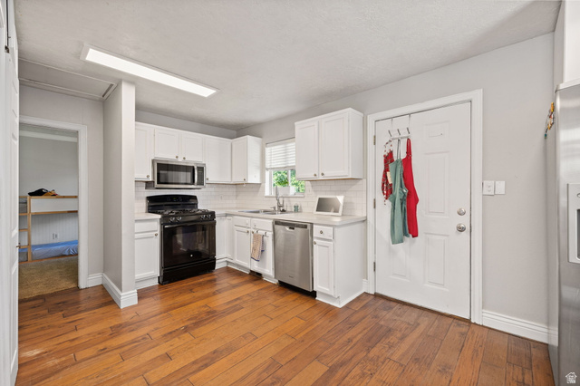 594 850 West Provo, UT 84601 - Photo 6 of 33 Kitchen featuring wood-finish flooring, white cabinetry, a white subway tile backsplash, stainless steel dishwasher, and an over-the-range microwave