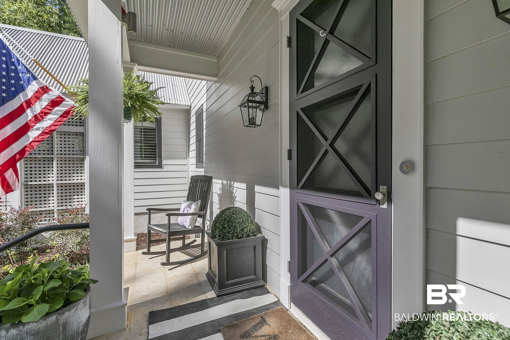 1106 Old County Road Daphne, AL 36526 - Photo 62 of 66 Covered porch entry featuring a dark-toned screen door with X-pattern detailing, horizontal siding, black exterior lantern, and corrugated metal roofing
