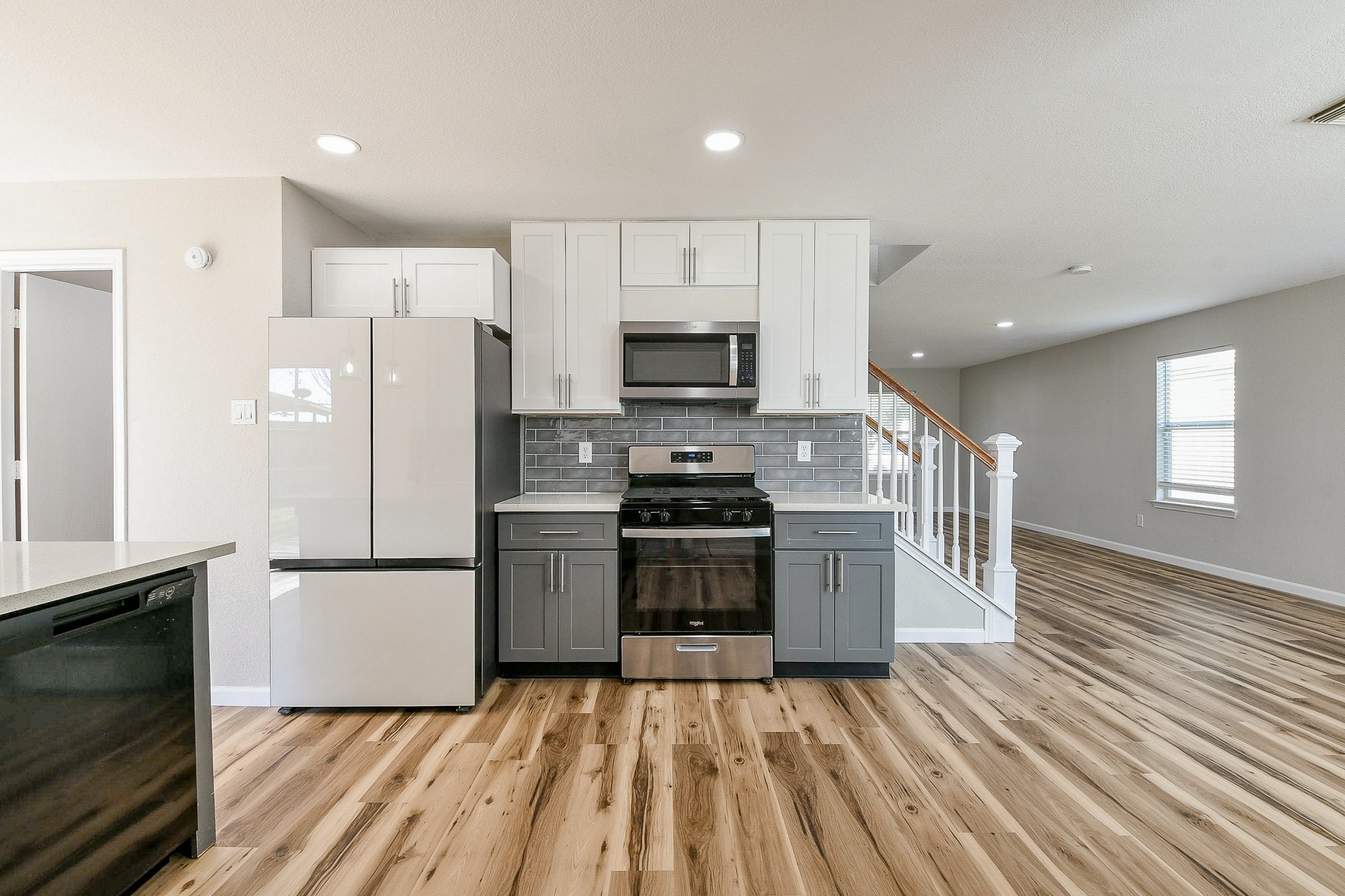 20807 Lansing Ridge Lane Katy, TX 77449 - Photo 11 of 35 Modern kitchen with two-tone cabinets and stainless steel appliances, featuring a sleek wood floor. Open layout leads to a staircase and bright living area with ample natural light.