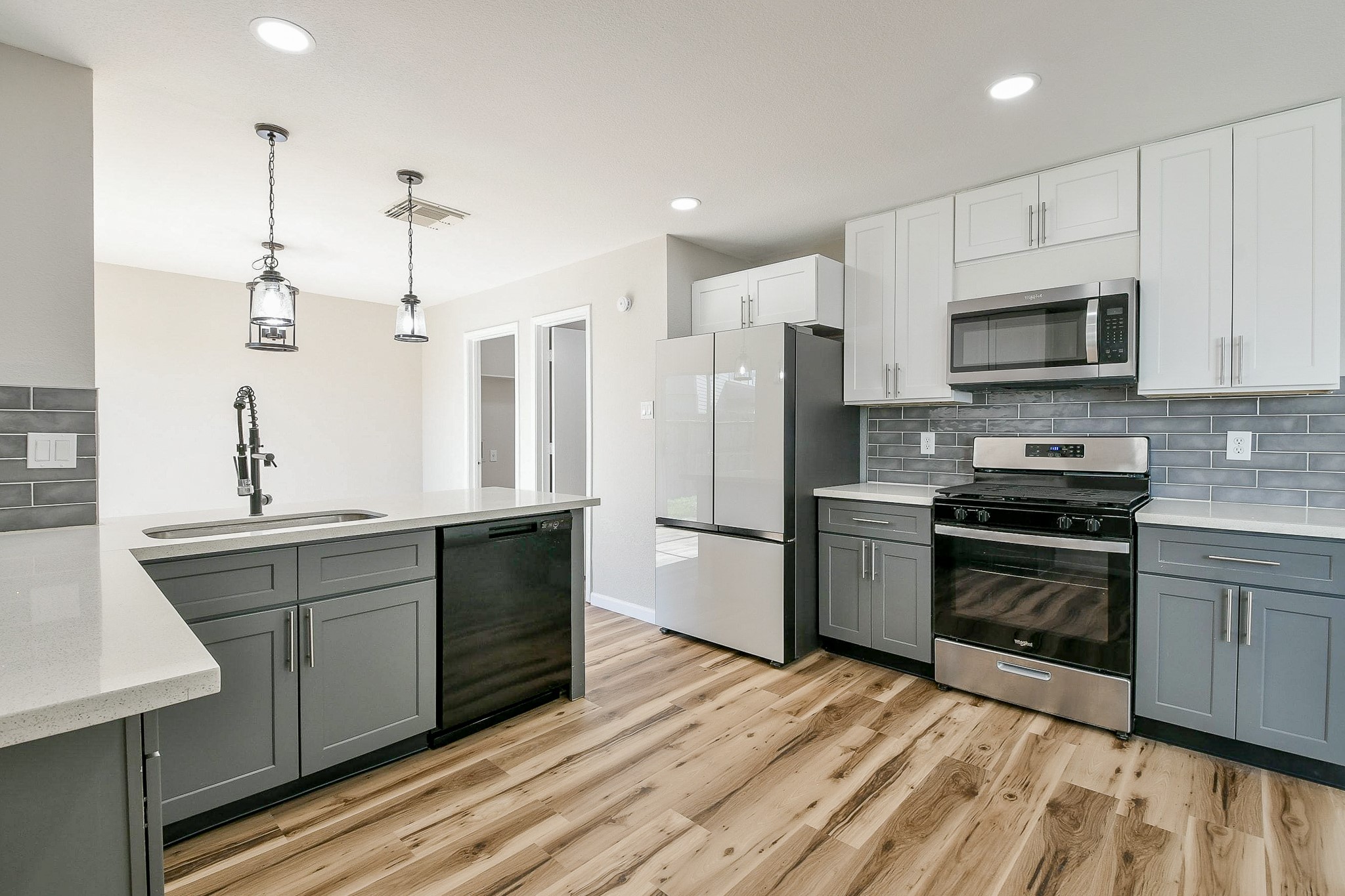 20807 Lansing Ridge Lane Katy, TX 77449 - Photo 12 of 35 This kitchen features modern stainless steel appliances, a stylish grey and white color scheme, quartz countertops, and wood-look flooring, creating a bright and contemporary space.