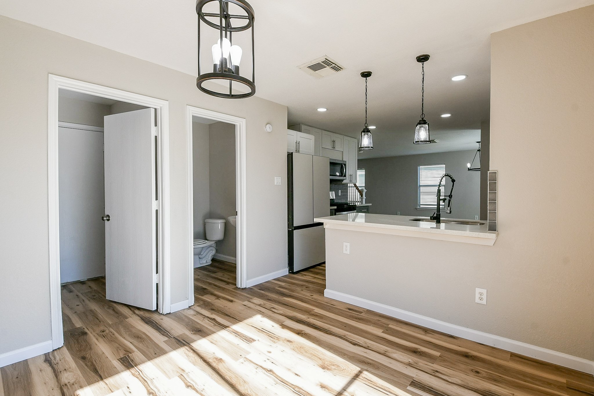 20807 Lansing Ridge Lane Katy, TX 77449 - Photo 14 of 35 Bright, modern kitchen with open layout, featuring wood floors, a breakfast bar, stainless steel appliances, and stylish pendant lighting. Adjacent to a bathroom and utility room, offering convenience and functionality.