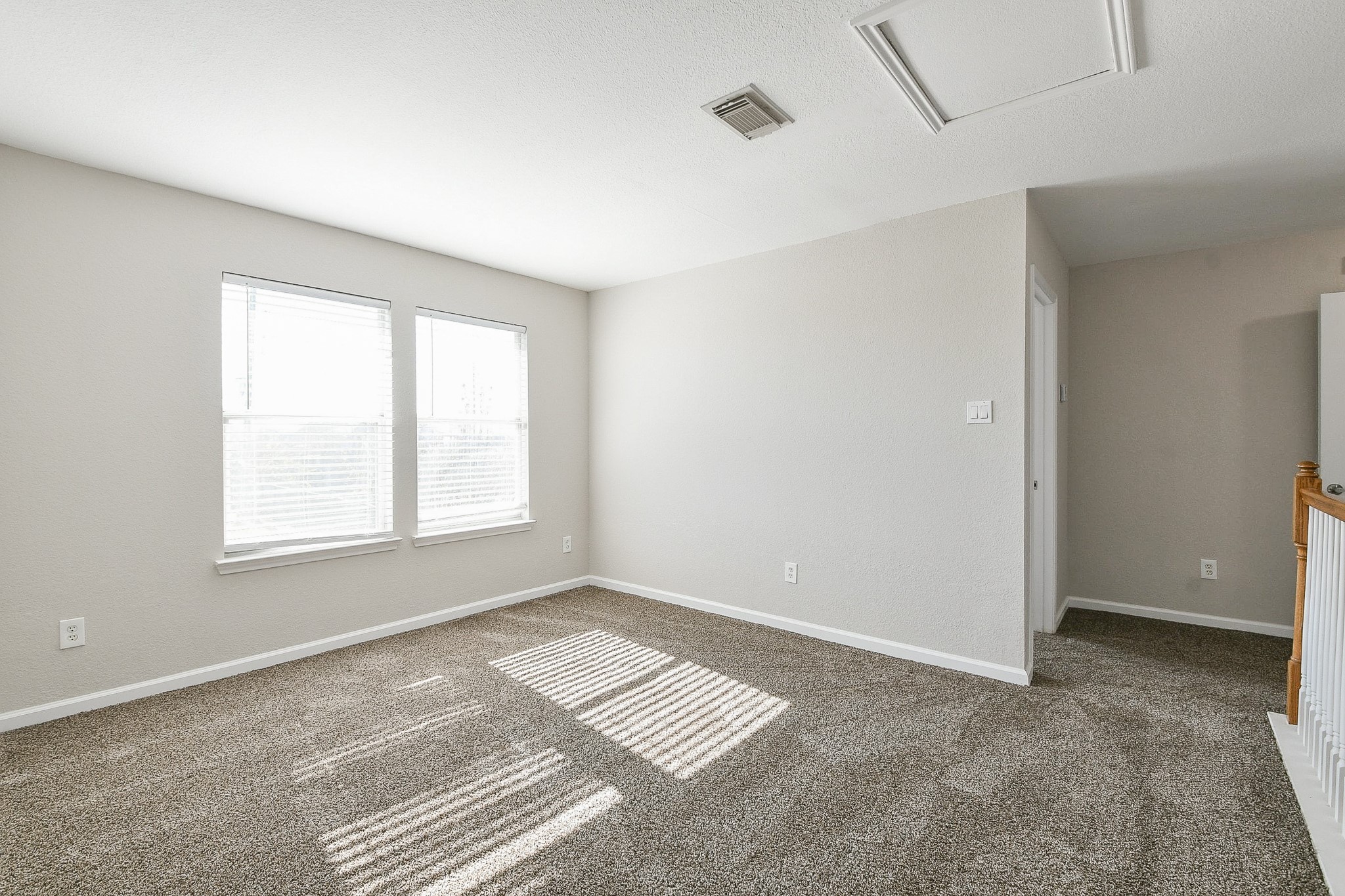 20807 Lansing Ridge Lane Katy, TX 77449 - Photo 19 of 35 This room features neutral walls, carpeted flooring, and ample natural light from two windows. It has a simple, clean design with a small hallway and railing leading to another area.