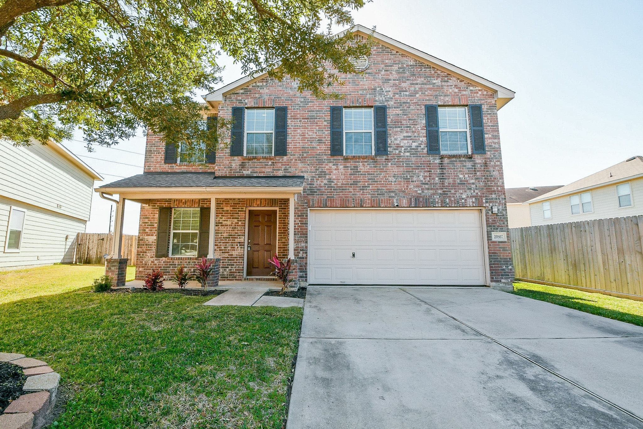 20807 Lansing Ridge Lane Katy, TX 77449 - Photo 2 of 35 This is a two-story brick home with a two-car garage. It features a neat front yard with a large tree providing shade, and a welcoming covered entryway. The exterior is enhanced by black shutters and a well-maintained driveway and newly painted front door.