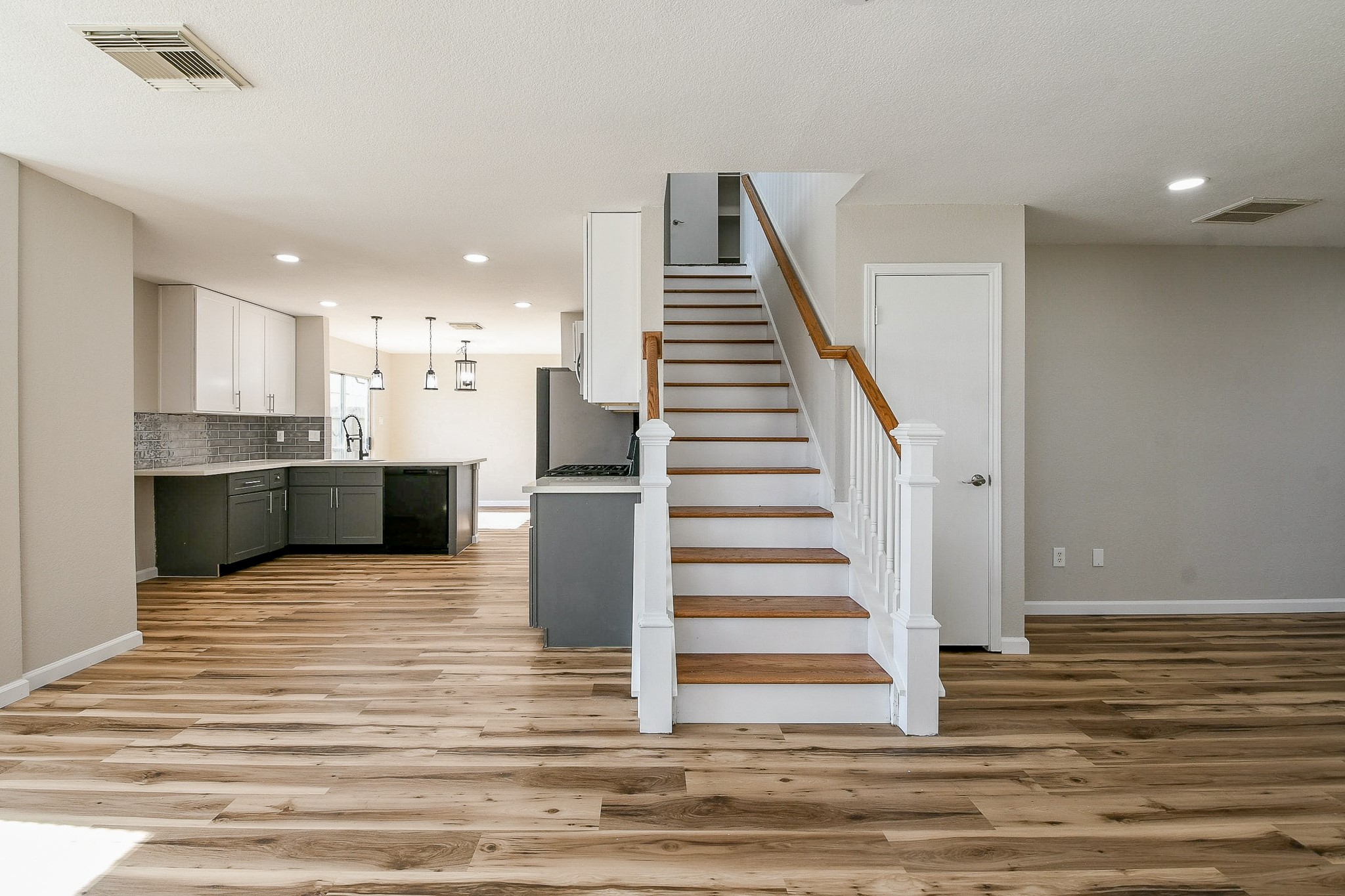 20807 Lansing Ridge Lane Katy, TX 77449 - Photo 35 of 35 This photo features a modern interior with an open floor plan, showcasing a stylish kitchen with dark cabinets, light countertops, and pendant lighting. The space has warm wood flooring, a central staircase with white railings, and ample natural light.