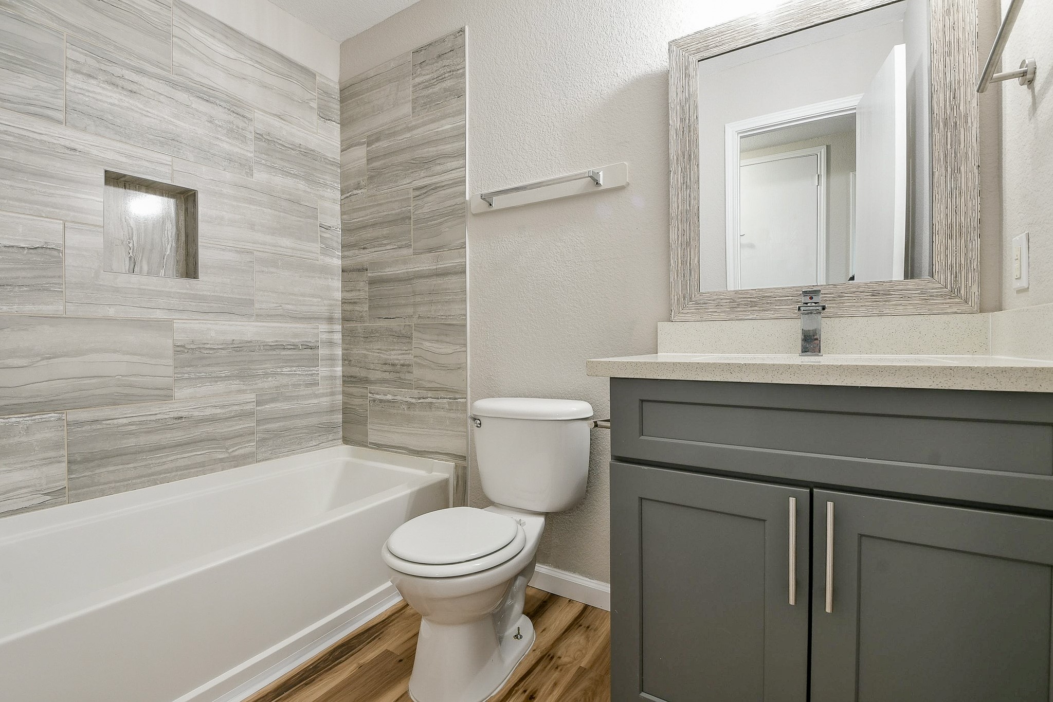 20807 Lansing Ridge Lane Katy, TX 77449 - Photo 22 of 35 This secondary bathroom features a modern design with a sleek gray vanity and a large mirror. It includes a bathtub with elegant gray tile surround and wood-like flooring, creating a clean and inviting space.