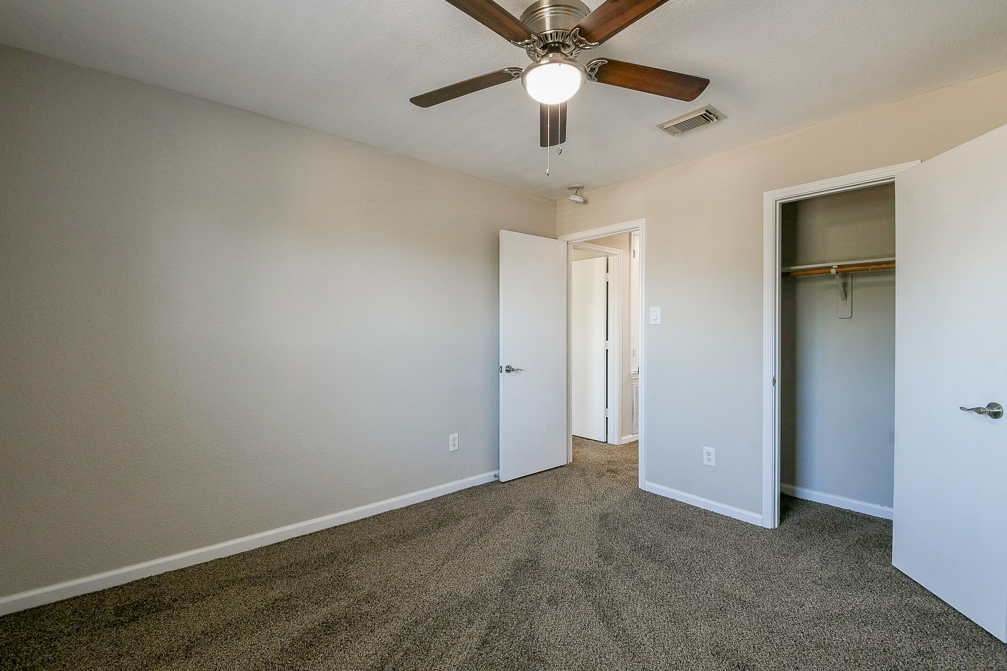 20807 Lansing Ridge Lane Katy, TX 77449 - Photo 24 of 35 This photo shows a cozy, freshly painted bedroom with neutral walls and carpet flooring. It features a ceiling fan, a small closet, and a door leading to the hallway.