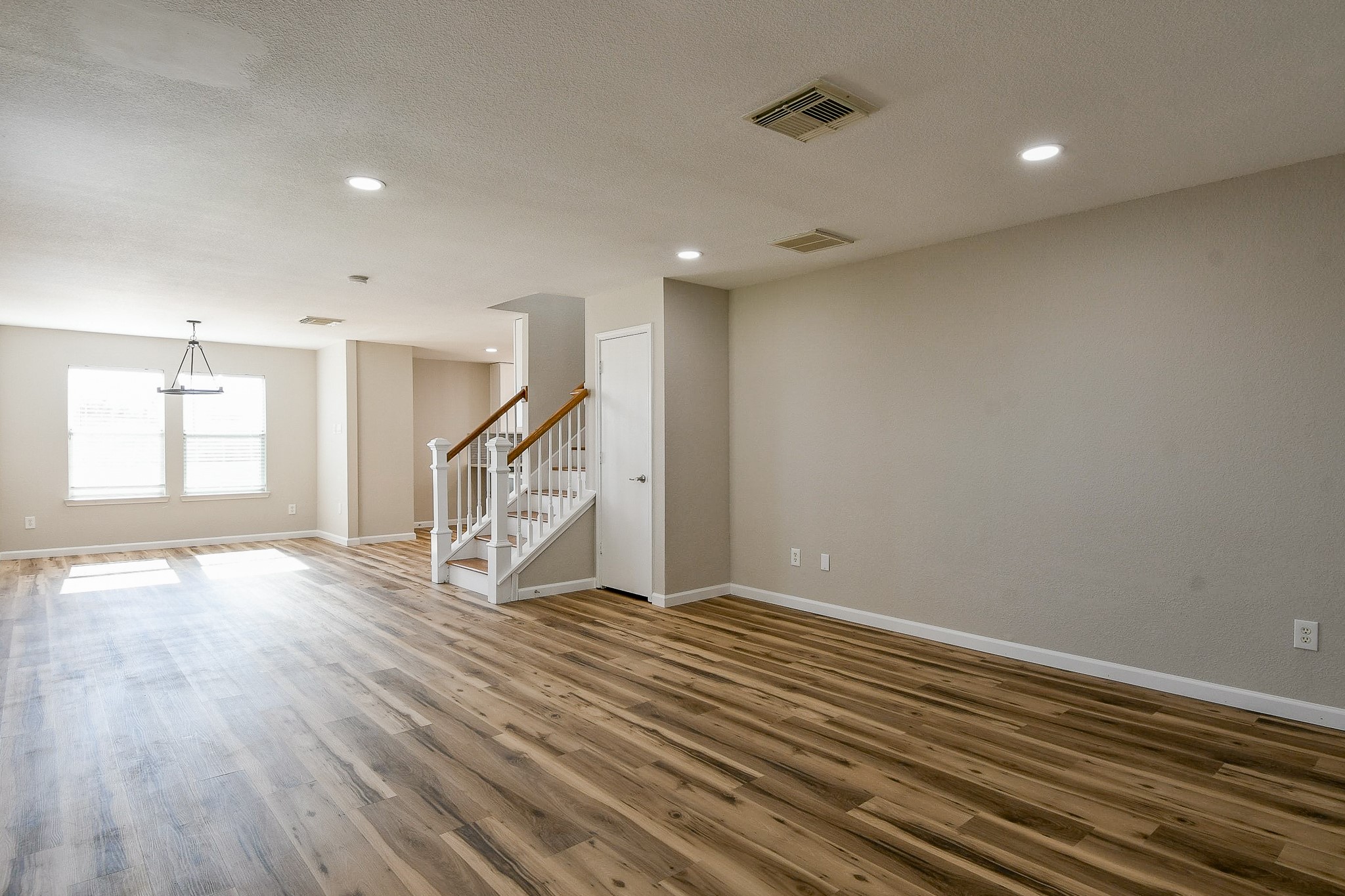 20807 Lansing Ridge Lane Katy, TX 77449 - Photo 4 of 35 This spacious open-concept living area features modern recessed lighting and elegant wood flooring. A staircase with a white railing adds a touch of charm, and large windows offer abundant natural light. Ideal for comfortable living and entertaining.