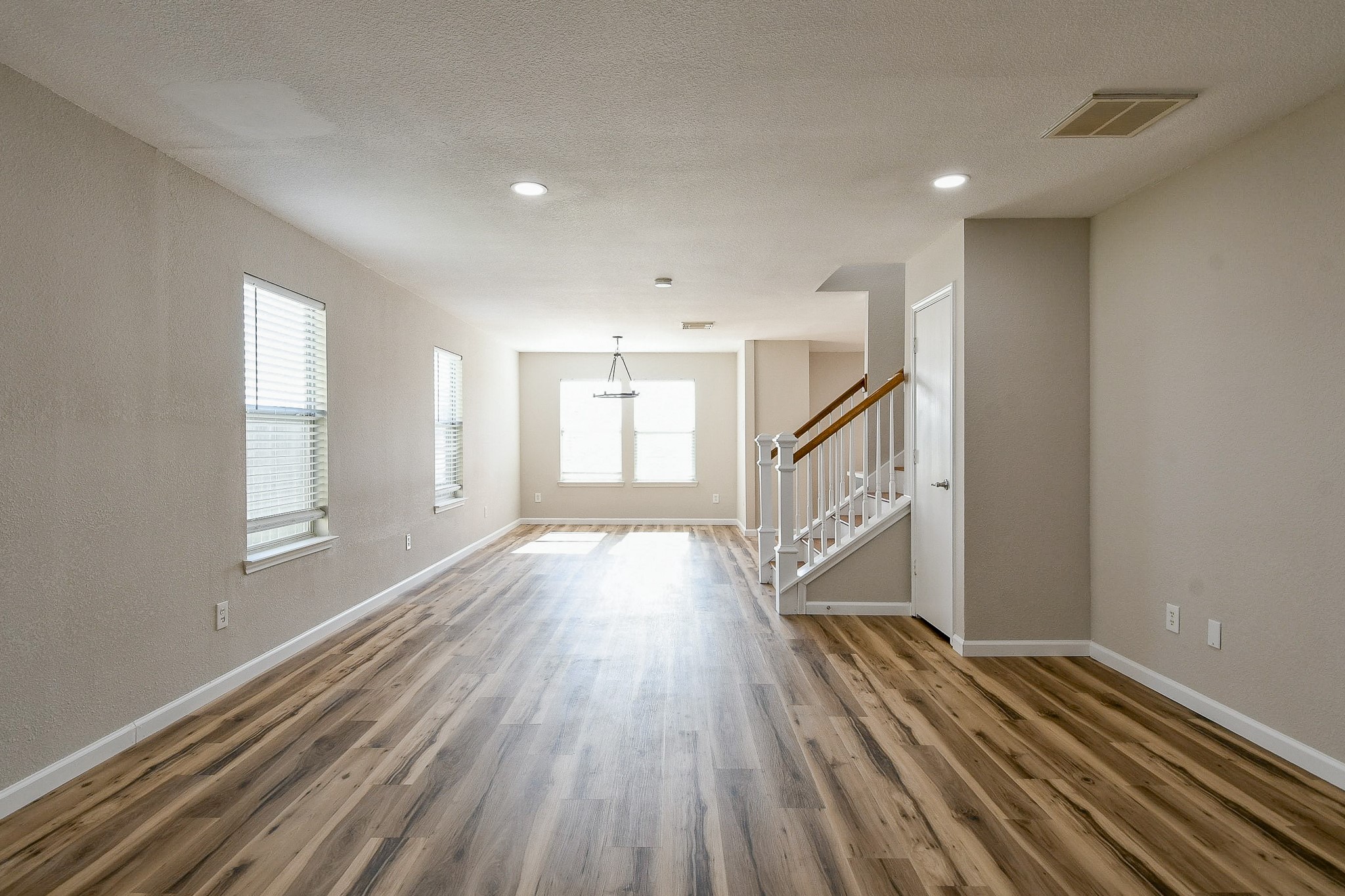 20807 Lansing Ridge Lane Katy, TX 77449 - Photo 5 of 35 This photo shows a spacious, well-lit living area and dining area with light wood flooring and neutral walls. Large windows allow natural light to fill the space, and a modern light fixture enhances the room. A staircase with a white railing leads to the upper level, adding character and functionality.