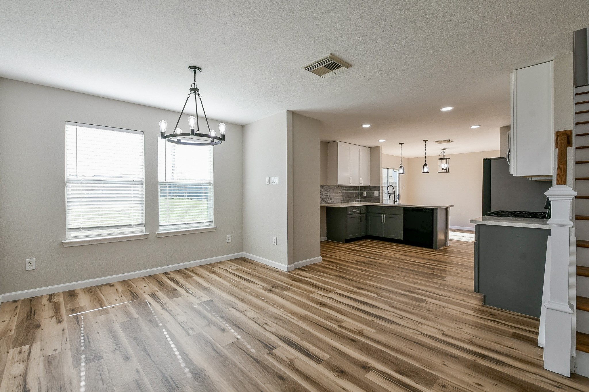 20807 Lansing Ridge Lane Katy, TX 77449 - Photo 7 of 35 Bright and open living space with modern wood flooring, featuring a contemporary light fixture. The kitchen boasts sleek cabinetry, a large island, and pendant lighting. Stairs lead to the upper level, adding a touch of elegance. Large windows provide ample natural light.