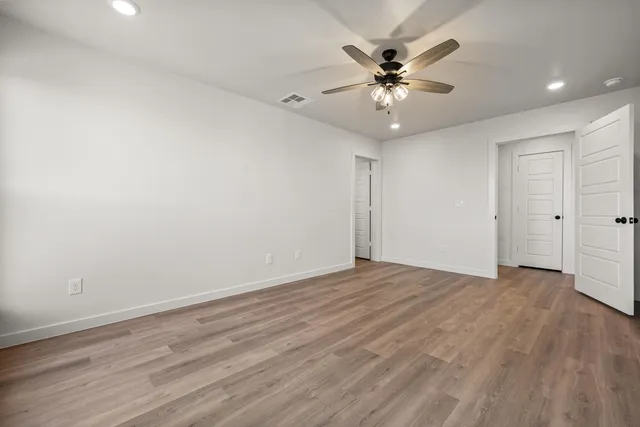an empty room with wooden floor fan and windows