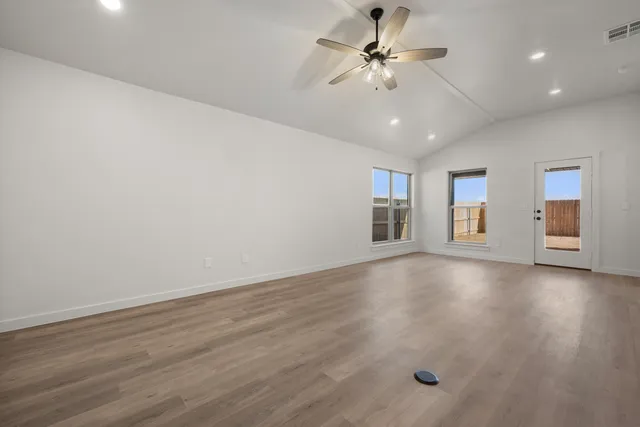 a view of an empty room with chandelier fan and wooden floor