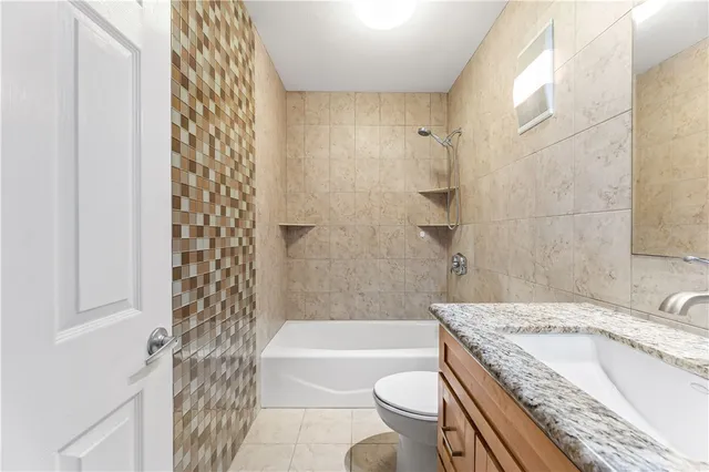 a bathroom with a granite countertop bathtub sink vanity mirror and toilet