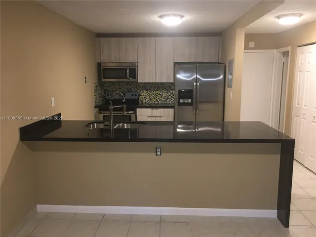 a kitchen with granite countertop a refrigerator a sink and chairs