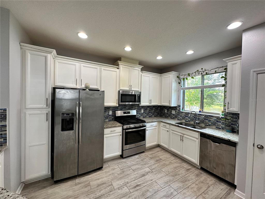 250 Rustic Loop Sanford, FL 32771 - Photo 7 of 33 a kitchen with stainless steel appliances granite countertop a refrigerator a sink dishwasher a stove and white cabinets with wooden floor