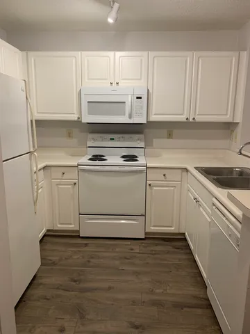 a white kitchen with granite countertop a stove top oven a sink and white cabinets