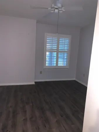 an empty room with wooden floor chandelier fan and windows