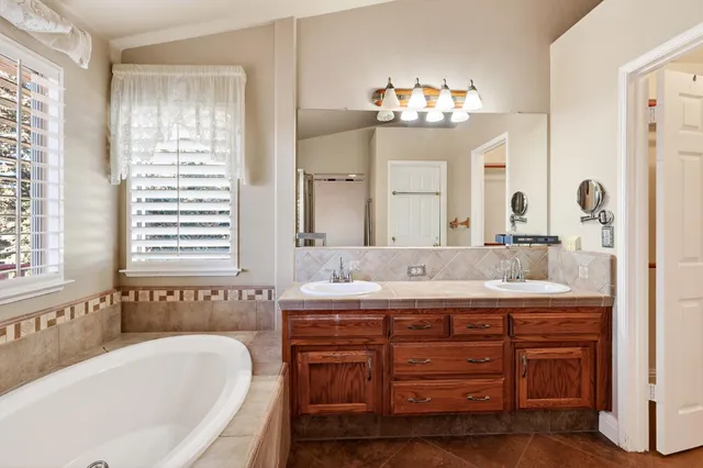a bathroom with a granite countertop sink a large mirror and a bathtub next to a window