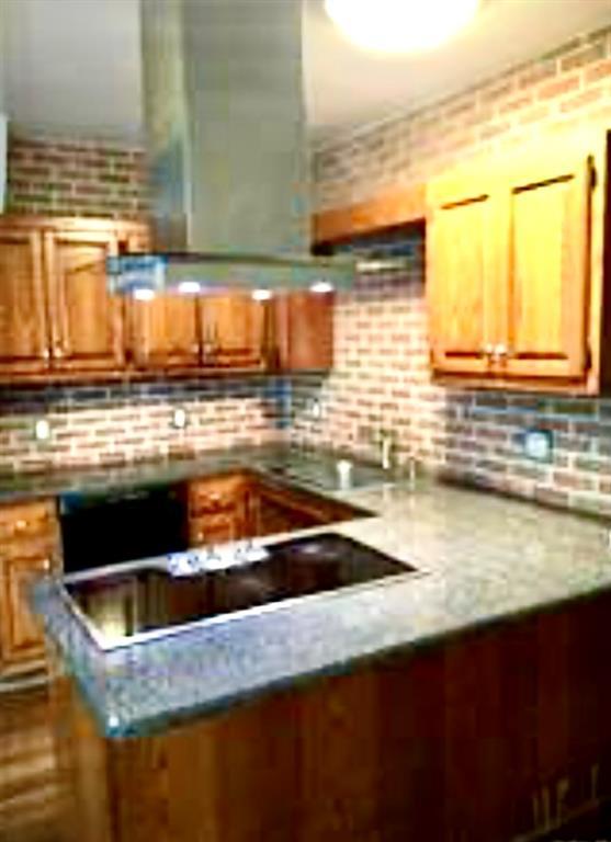 Kitchen with brown cabinetry, decorative backsplash, oven, and light stone countertops