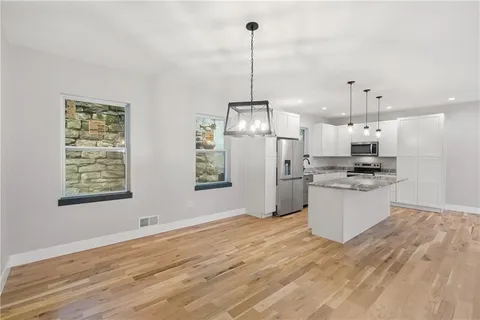 a open kitchen with stainless steel appliances kitchen island granite countertop a refrigerator a oven a white stove with white cabinets and wooden floor