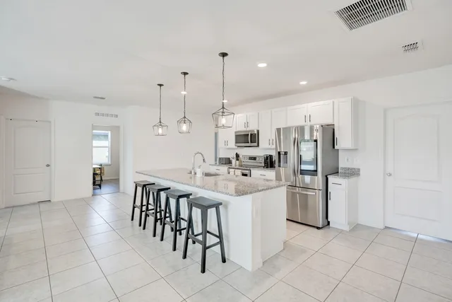 a kitchen with stainless steel appliances kitchen island granite countertop a refrigerator a stove a sink and white cabinets