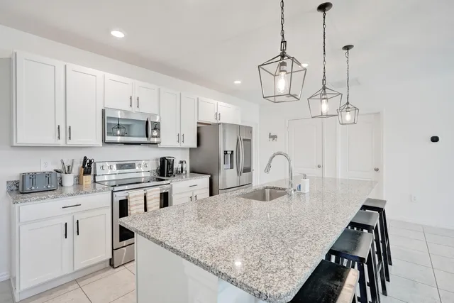 a kitchen with stainless steel appliances granite countertop a stove top oven a sink a refrigerator and white cabinets