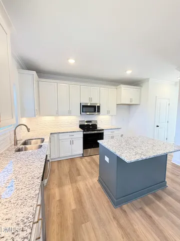 a large kitchen with granite countertop a stove top oven a sink dishwasher and white cabinets with wooden floor