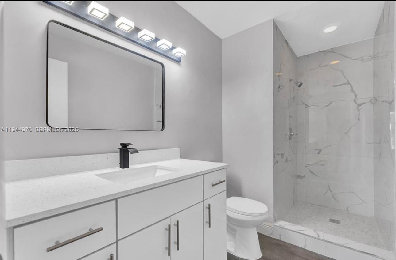 7402 Northwest 75th Street Tamarac, FL 33321 - Photo 29 of 38 a bathroom with a toilet a sink a mirror a vanity and shower