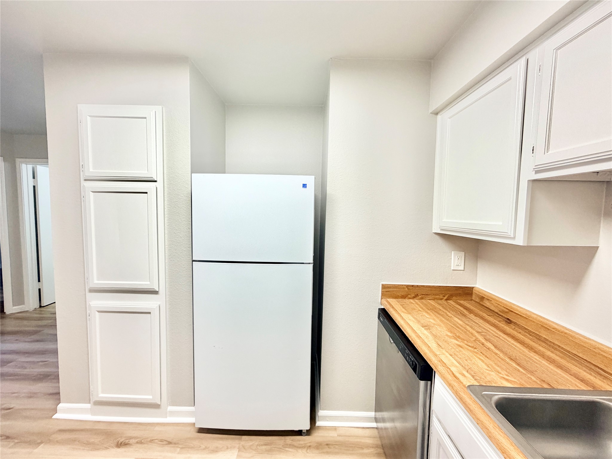 1730 Timber Ridge Road, Unit 152 Austin, TX 78741 - Photo 16 of 26 Kitchen featuring light countertops, freestanding refrigerator, stainless steel dishwasher, white cabinets, and light wood-type flooring