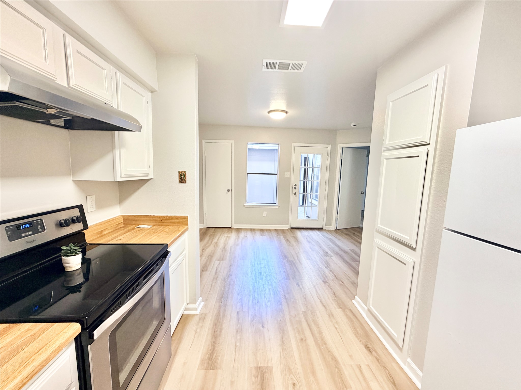 1730 Timber Ridge Road, Unit 152 Austin, TX 78741 - Photo 17 of 26 Kitchen with electric range, freestanding refrigerator, white cabinets, light wood-style flooring, and under cabinet range hood