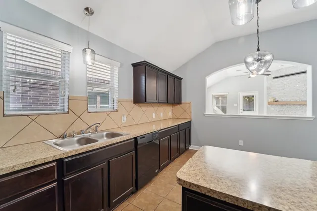 a kitchen with stainless steel appliances granite countertop wooden cabinets a sink dishwasher a stove and a dining table with wooden floor