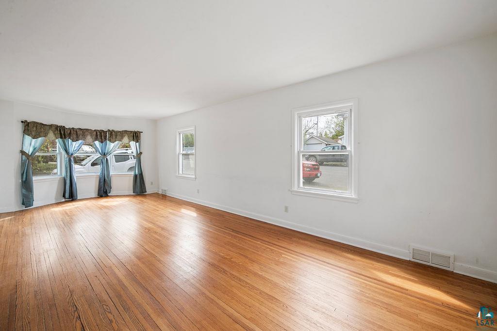122 3rd Street Cloquet, MN 55720 - Photo 3 of 42 Spacious room featuring wood-finish flooring, white walls, and multiple windows including a bay window
