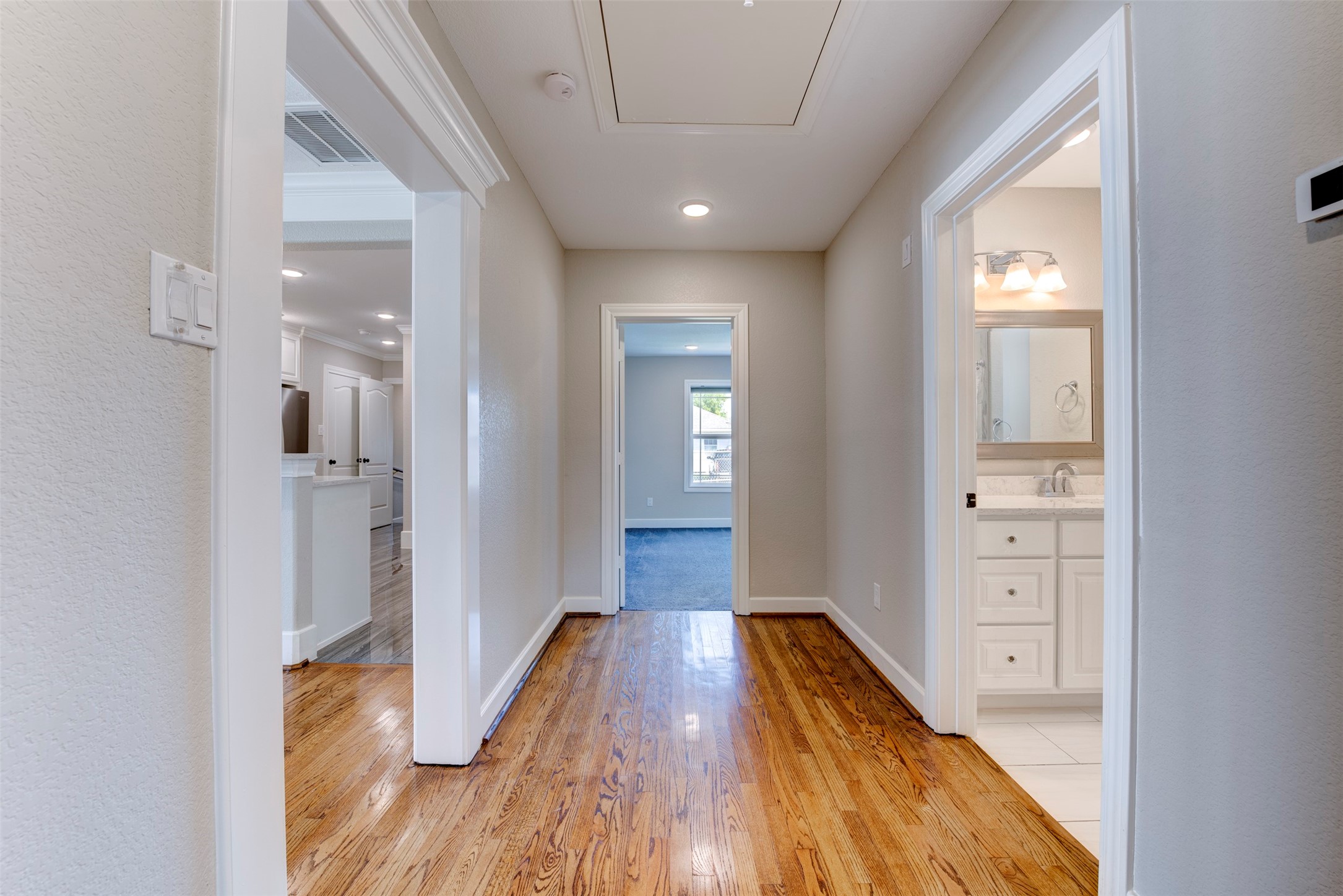 109 Dresden Street Houston, TX 77012 - Photo 30 of 43 Bright hallway with polished hardwood floors leading to a carpeted room, visible bathroom, and an open kitchen area. Neutral walls and recessed lighting provide a modern, clean look.