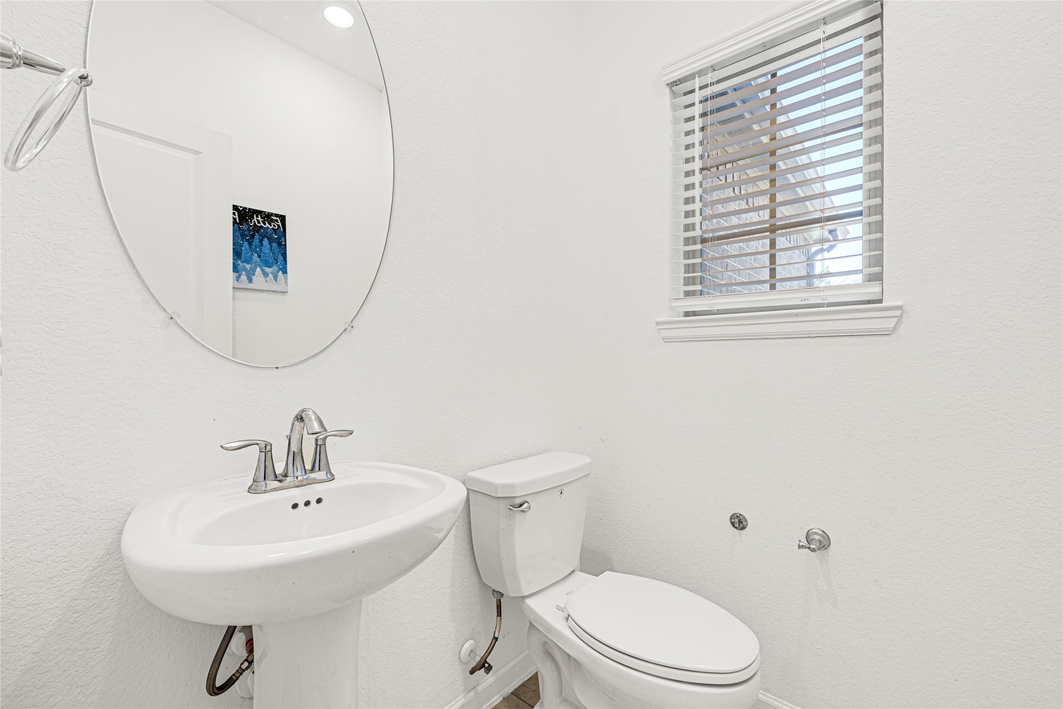 4307 Annandale Lane Rosharon, TX 77583 - Photo 8 of 31 This photo shows the bright, half bathroom on the first floor with a white pedestal sink, a toilet, and a round mirror. It features a window with blinds, allowing natural light to enter, and has a clean, modern look.