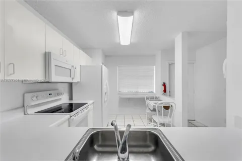a room with kitchen island a sink a stove and white cabinets
