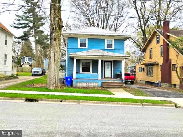 a view of a white house with a large tree and plants