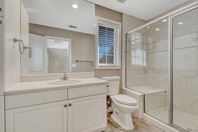 a bathroom with a toilet sink vanity granite and shower
