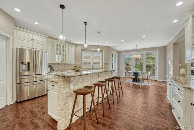 a kitchen with stainless steel appliances granite countertop a stove a refrigerator a kitchen island a dining table and chairs with wooden floor
