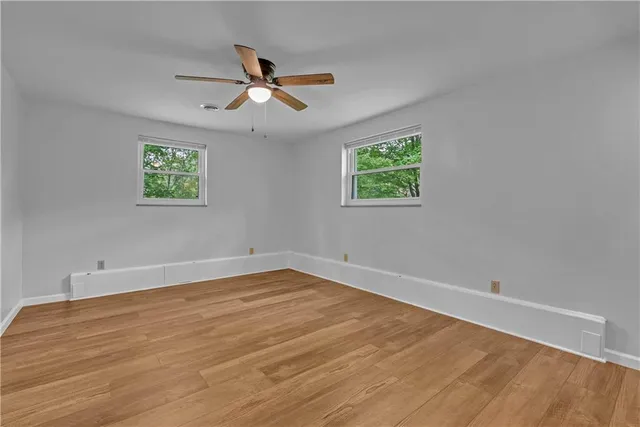 an empty room with wooden floor ceiling fan and windows